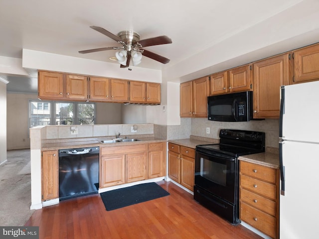 kitchen featuring a peninsula, wood finished floors, black appliances, a ceiling fan, and a sink