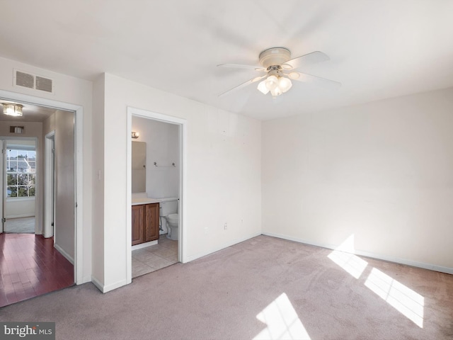 unfurnished bedroom featuring visible vents, connected bathroom, baseboards, light colored carpet, and ceiling fan