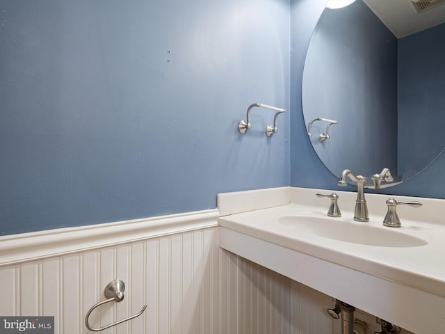 bathroom with a wainscoted wall, visible vents, and a sink