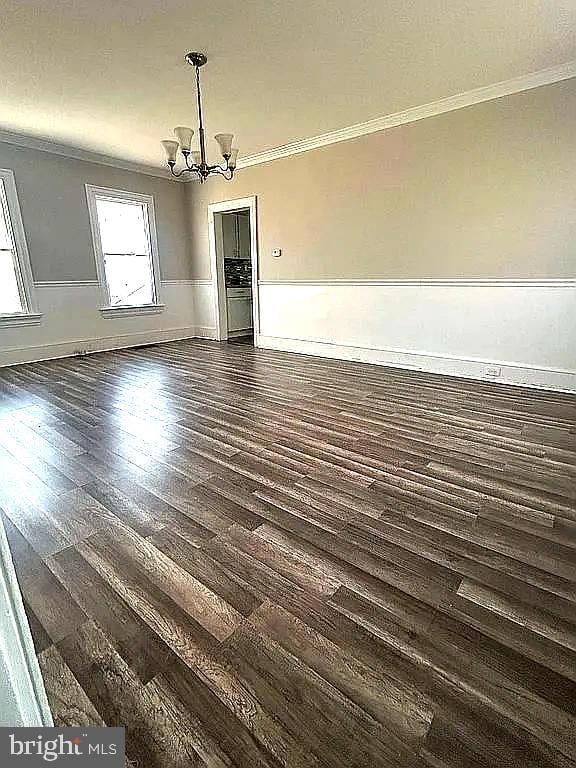 unfurnished dining area with dark hardwood / wood-style floors, crown molding, and an inviting chandelier