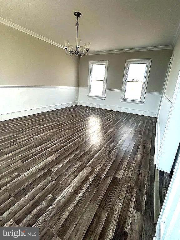 unfurnished dining area with ornamental molding, dark wood-type flooring, and a notable chandelier