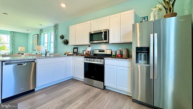 kitchen with light stone countertops, white cabinetry, sink, appliances with stainless steel finishes, and light wood-type flooring