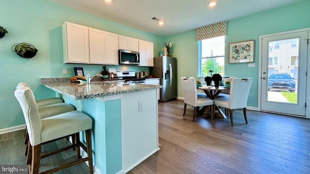 kitchen featuring white cabinets, dark hardwood / wood-style floors, appliances with stainless steel finishes, light stone counters, and kitchen peninsula