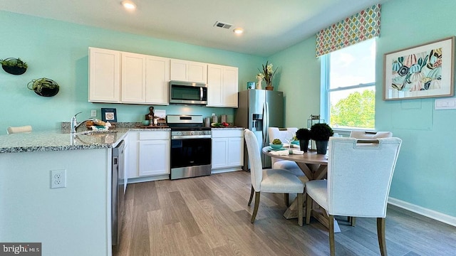 kitchen with sink, light wood-type flooring, appliances with stainless steel finishes, light stone counters, and white cabinetry