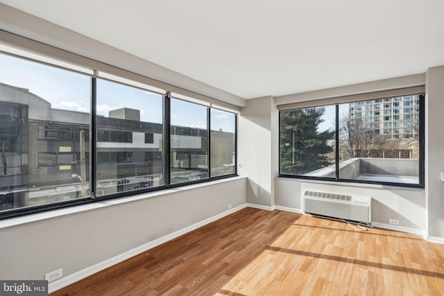 spare room featuring a wall mounted air conditioner, wood-type flooring, and a wealth of natural light