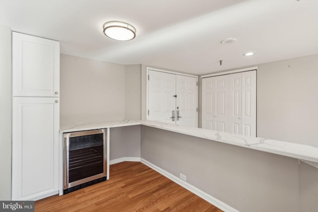 bar featuring light stone counters, light wood-type flooring, and beverage cooler