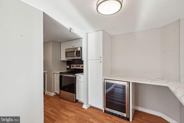 kitchen featuring white cabinets, wine cooler, light wood-type flooring, appliances with stainless steel finishes, and light stone counters