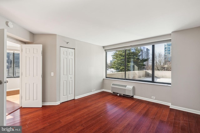 empty room with a wall unit AC and dark wood-type flooring