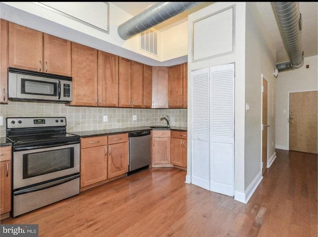 kitchen with sink, a towering ceiling, light wood-type flooring, and appliances with stainless steel finishes