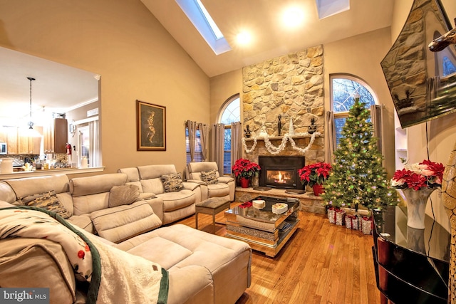 living room with a fireplace, light hardwood / wood-style floors, high vaulted ceiling, and a skylight