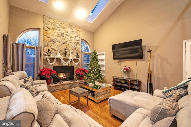 living room with a stone fireplace, hardwood / wood-style floors, high vaulted ceiling, and a skylight