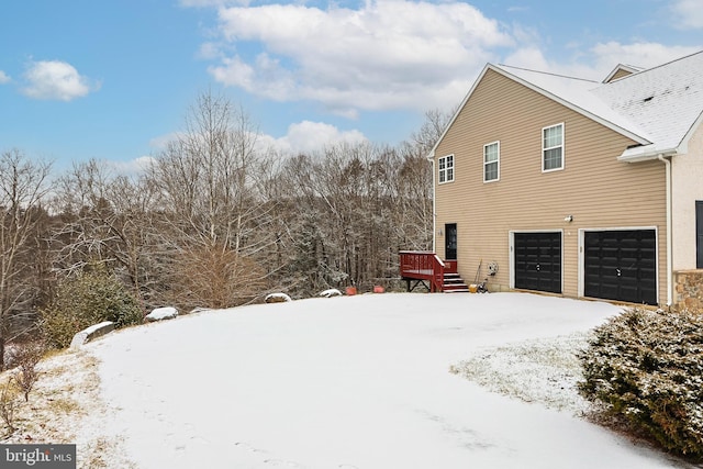 snow covered property with a wooden deck and a garage