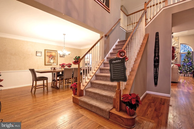 staircase featuring wood-type flooring, crown molding, and a notable chandelier