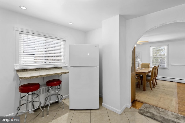 kitchen with white refrigerator, a kitchen bar, light tile patterned floors, and baseboard heating