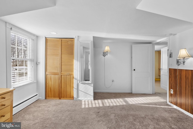 interior space with light carpet, a closet, wood walls, and a baseboard heating unit