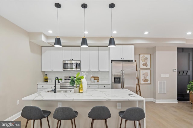 kitchen featuring appliances with stainless steel finishes, an island with sink, decorative light fixtures, and sink