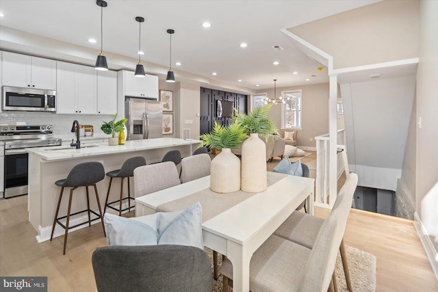 dining area with light wood-type flooring, a notable chandelier, and sink