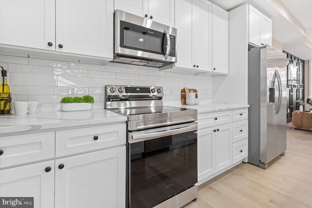 kitchen featuring white cabinetry, appliances with stainless steel finishes, tasteful backsplash, light wood-type flooring, and light stone counters