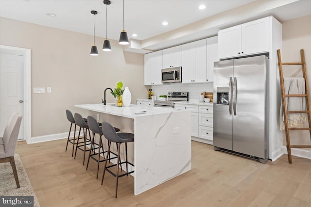 kitchen with tasteful backsplash, white cabinetry, hanging light fixtures, appliances with stainless steel finishes, and an island with sink