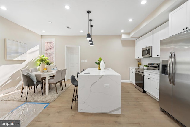 kitchen featuring light stone countertops, white cabinets, a kitchen island, decorative light fixtures, and stainless steel appliances