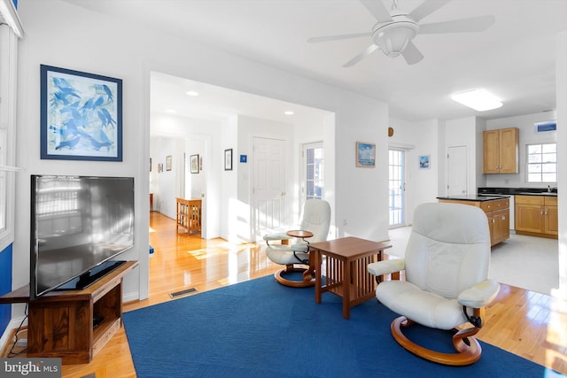 living room with light hardwood / wood-style flooring, ceiling fan, and a healthy amount of sunlight