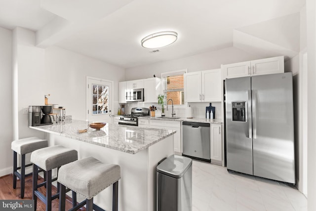 kitchen with stainless steel appliances, a breakfast bar, light stone counters, sink, and white cabinetry