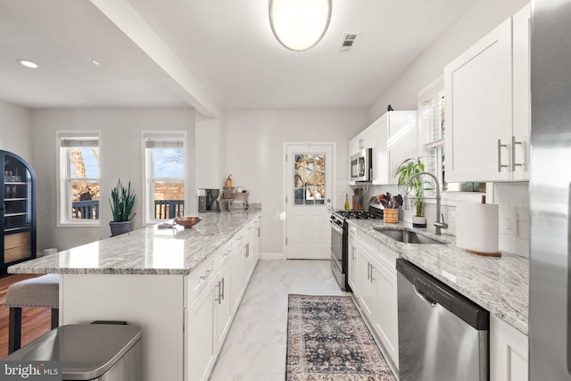 kitchen featuring sink, white cabinets, light stone counters, a breakfast bar, and appliances with stainless steel finishes