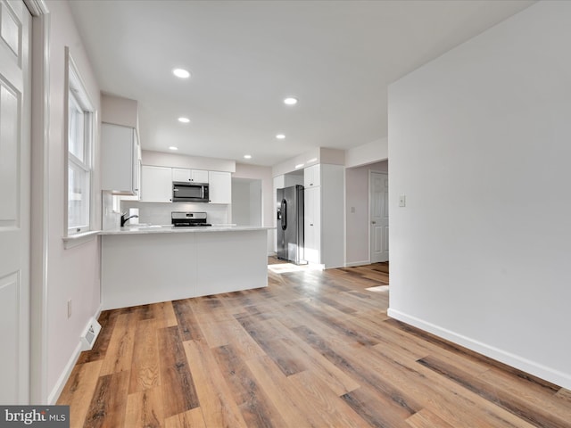 kitchen with stainless steel appliances, white cabinets, light hardwood / wood-style flooring, kitchen peninsula, and backsplash