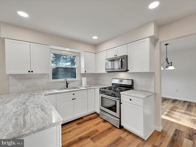 kitchen with stainless steel appliances, sink, decorative light fixtures, white cabinets, and light wood-type flooring