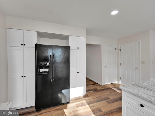 kitchen featuring light stone counters, white cabinets, black fridge with ice dispenser, and light wood-type flooring