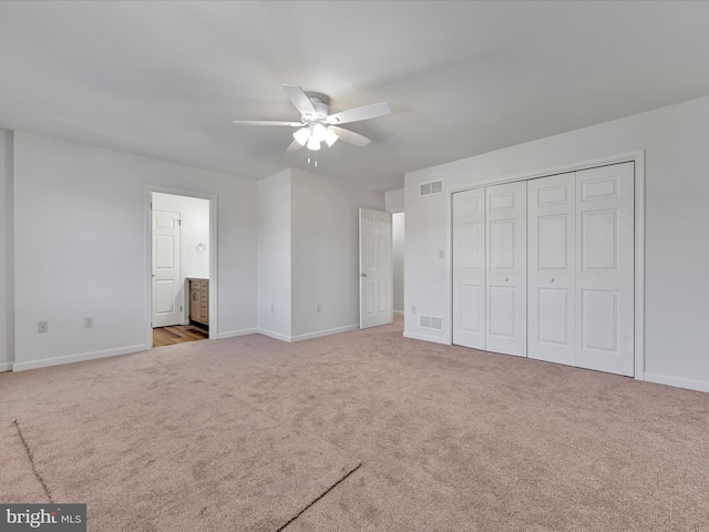 unfurnished bedroom featuring ceiling fan, ensuite bathroom, a closet, and light carpet