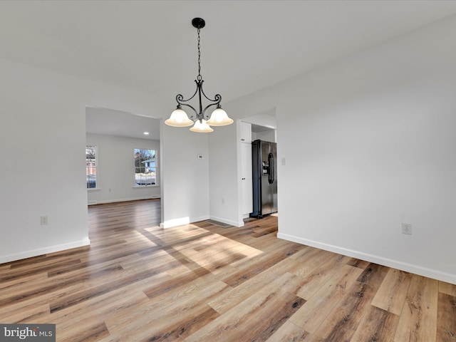 unfurnished dining area with an inviting chandelier and light wood-type flooring