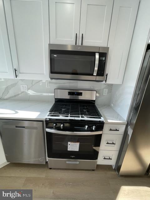 kitchen featuring tasteful backsplash, light stone countertops, white cabinets, and stainless steel appliances