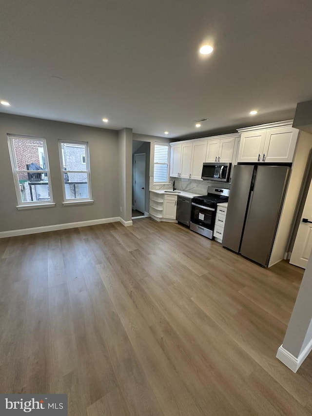 kitchen with decorative backsplash, white cabinets, stainless steel appliances, and light hardwood / wood-style floors