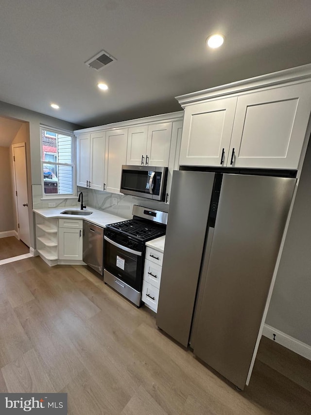 kitchen with white cabinets, light wood-type flooring, sink, and appliances with stainless steel finishes