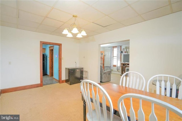 dining space with carpet flooring, a drop ceiling, and a notable chandelier