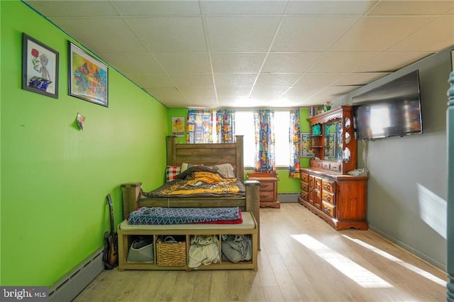 bedroom featuring light wood-type flooring, a drop ceiling, and a baseboard heating unit