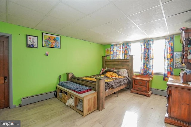 bedroom with a paneled ceiling, a baseboard radiator, and light hardwood / wood-style floors