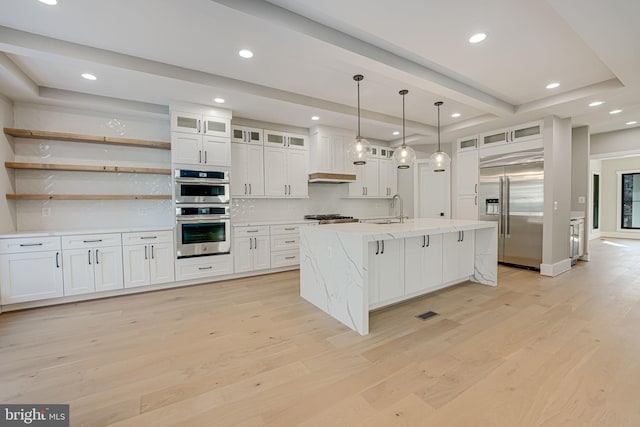 kitchen with appliances with stainless steel finishes, sink, white cabinets, hanging light fixtures, and light wood-type flooring