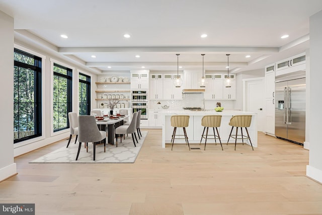 kitchen featuring a breakfast bar, hanging light fixtures, stainless steel appliances, an island with sink, and white cabinets