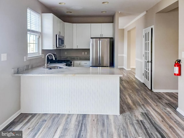 kitchen featuring white cabinetry, sink, kitchen peninsula, wood-type flooring, and appliances with stainless steel finishes