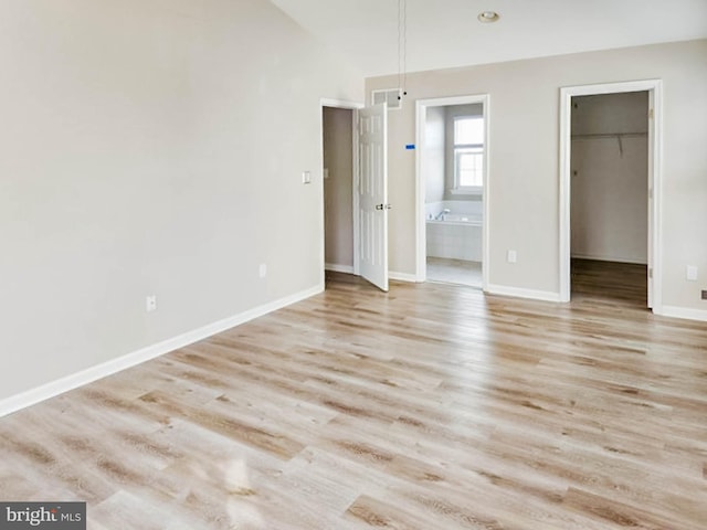 unfurnished bedroom featuring a spacious closet, connected bathroom, and light hardwood / wood-style flooring