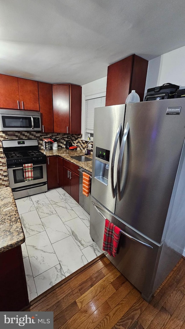 kitchen with stainless steel appliances, light stone counters, tasteful backsplash, and sink