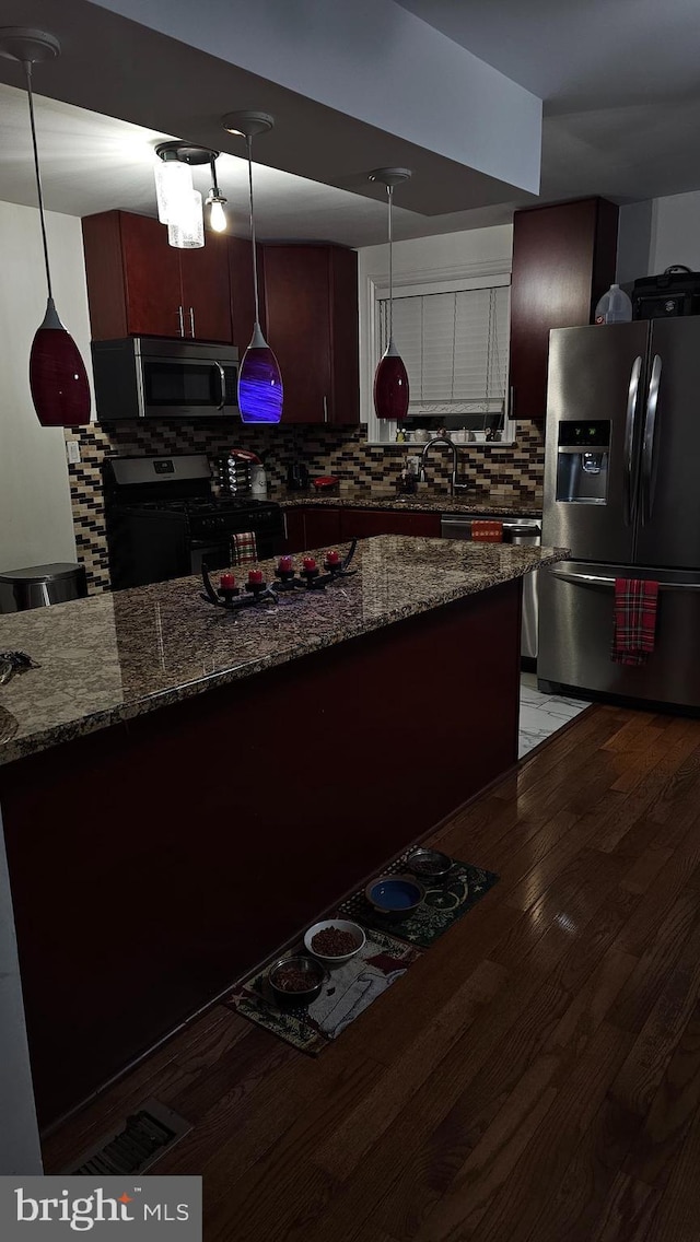 kitchen with dark stone counters, hardwood / wood-style flooring, decorative backsplash, decorative light fixtures, and stainless steel appliances