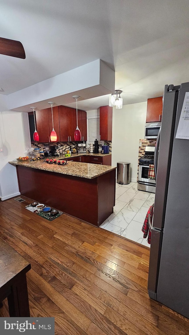 kitchen featuring kitchen peninsula, tasteful backsplash, light stone counters, stainless steel appliances, and pendant lighting