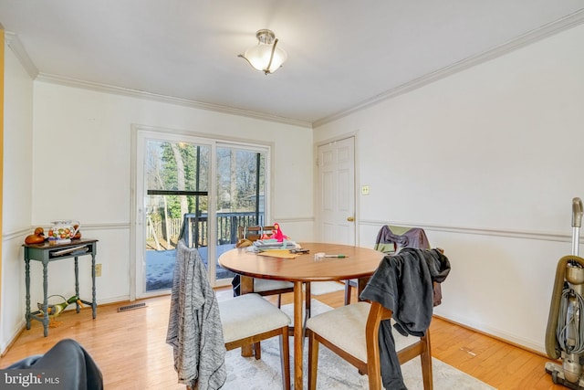 dining space with ornamental molding and light hardwood / wood-style flooring