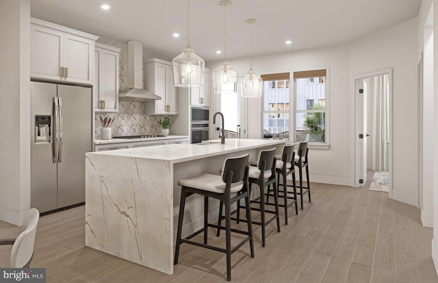 kitchen with tasteful backsplash, a kitchen island with sink, wall chimney range hood, white cabinets, and stainless steel fridge with ice dispenser