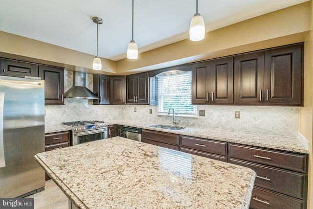 kitchen featuring dark brown cabinetry, sink, hanging light fixtures, wall chimney range hood, and appliances with stainless steel finishes