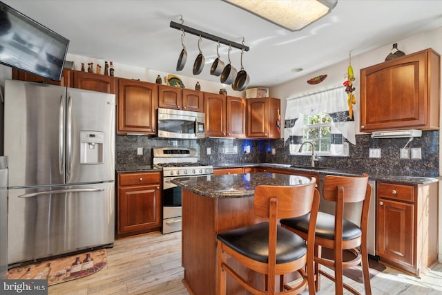 kitchen with a center island, track lighting, a kitchen breakfast bar, appliances with stainless steel finishes, and light hardwood / wood-style floors