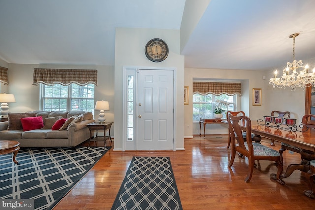 foyer entrance featuring lofted ceiling, wood-type flooring, a healthy amount of sunlight, and a notable chandelier